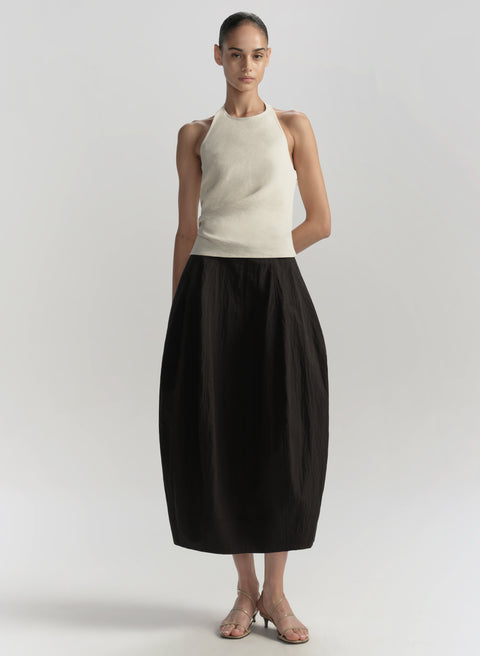 Woman wearing a high neck white sleeveless dress with a black balloon skirt