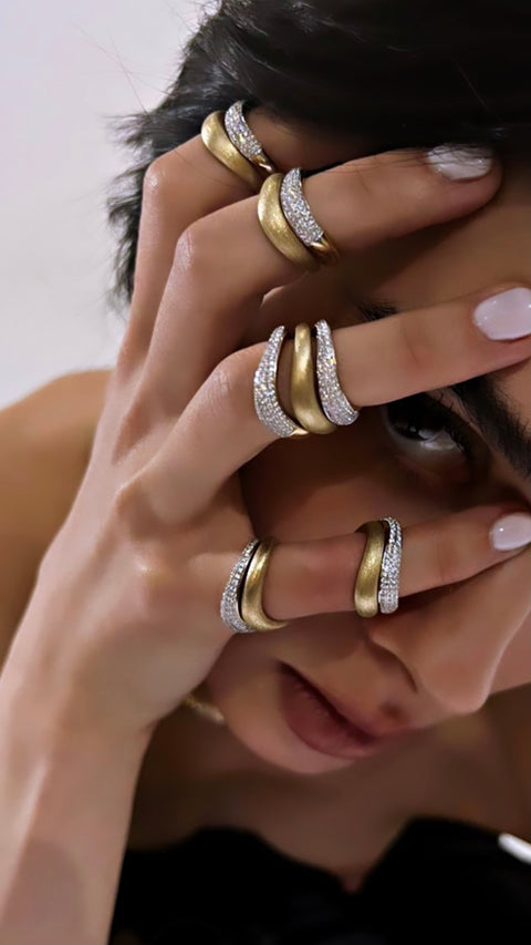 Model hand on head with yellow gold and diamond rings on every finger.