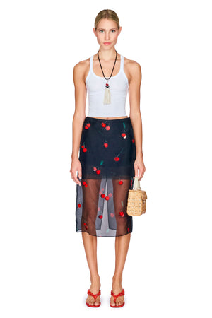 Woman wearing a white cropped tank top and black skirt with red cherry design on a white background