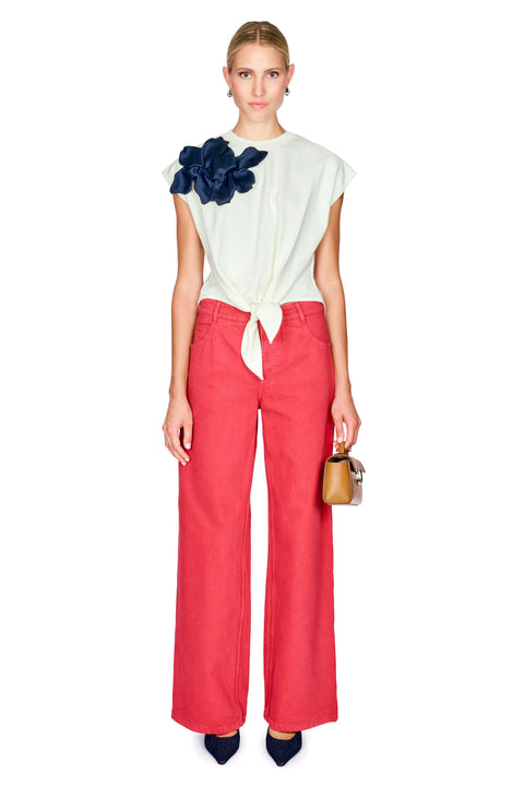 Woman wearing a white top with a navy floral detail and red pants on a white background