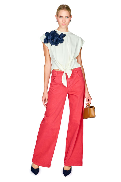 Woman wearing a white top with a navy floral detail and red pants on a white background