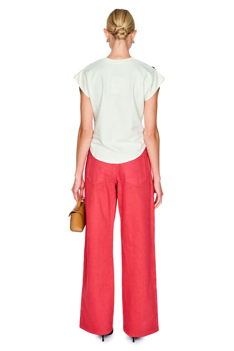 Woman wearing a white top with a navy floral detail and red pants on a white background back angle