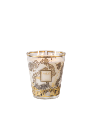 A ski-based candle in a clear glass vessel featuring a gold and brown mountain landscape illustration on a cream background, with a central gold label.