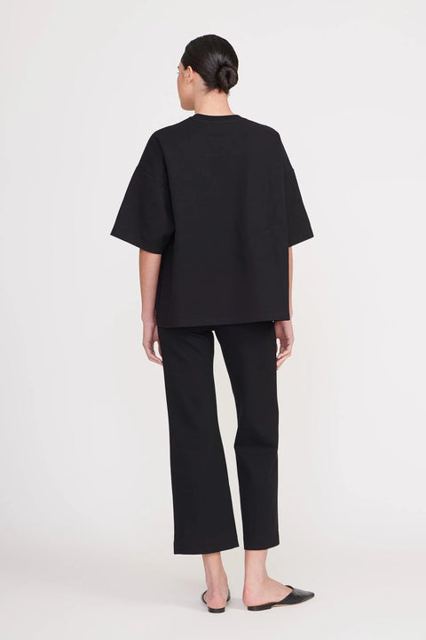 Back view of a woman wearing cropped black pants, paired with a matching oversized black t-shirt. 