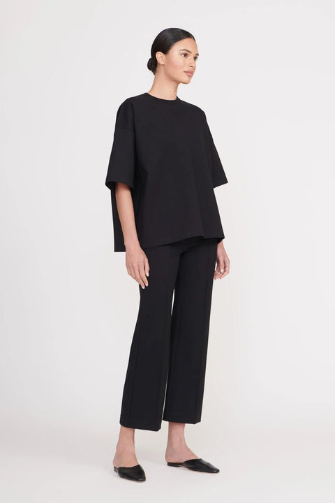 Side view of a woman wearing cropped black pants that feature a center seam down the front, paired with a matching oversized black t-shirt. 