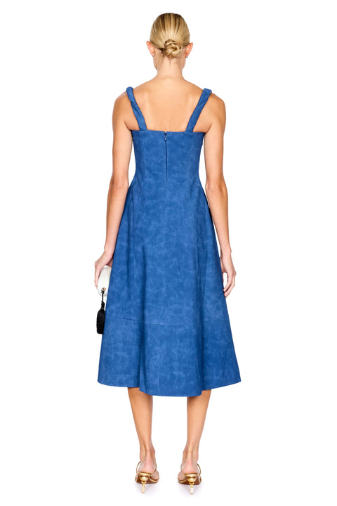 A woman viewed from the back wearing a sleeveless blue midi dress with shoulder straps and a gathered waist, standing against a plain white background.