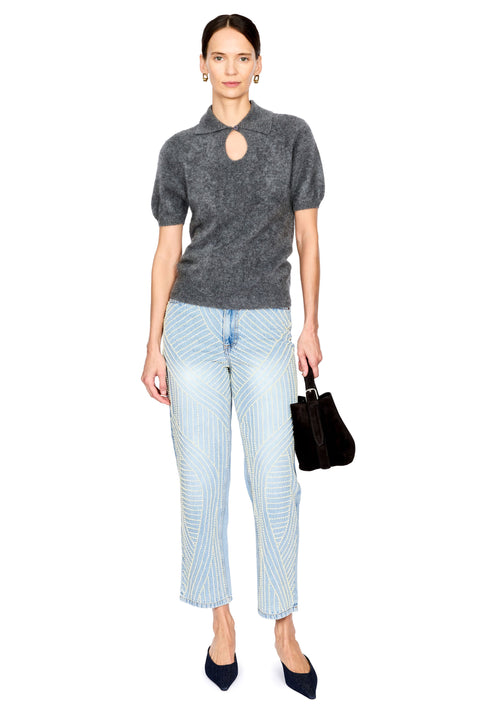 A model stands against a white background wearing a dark gray short-sleeve knit top with a keyhole cutout, light blue jeans with pearl detail, dark navy pointed shoes, and holding a dark brown handbag.