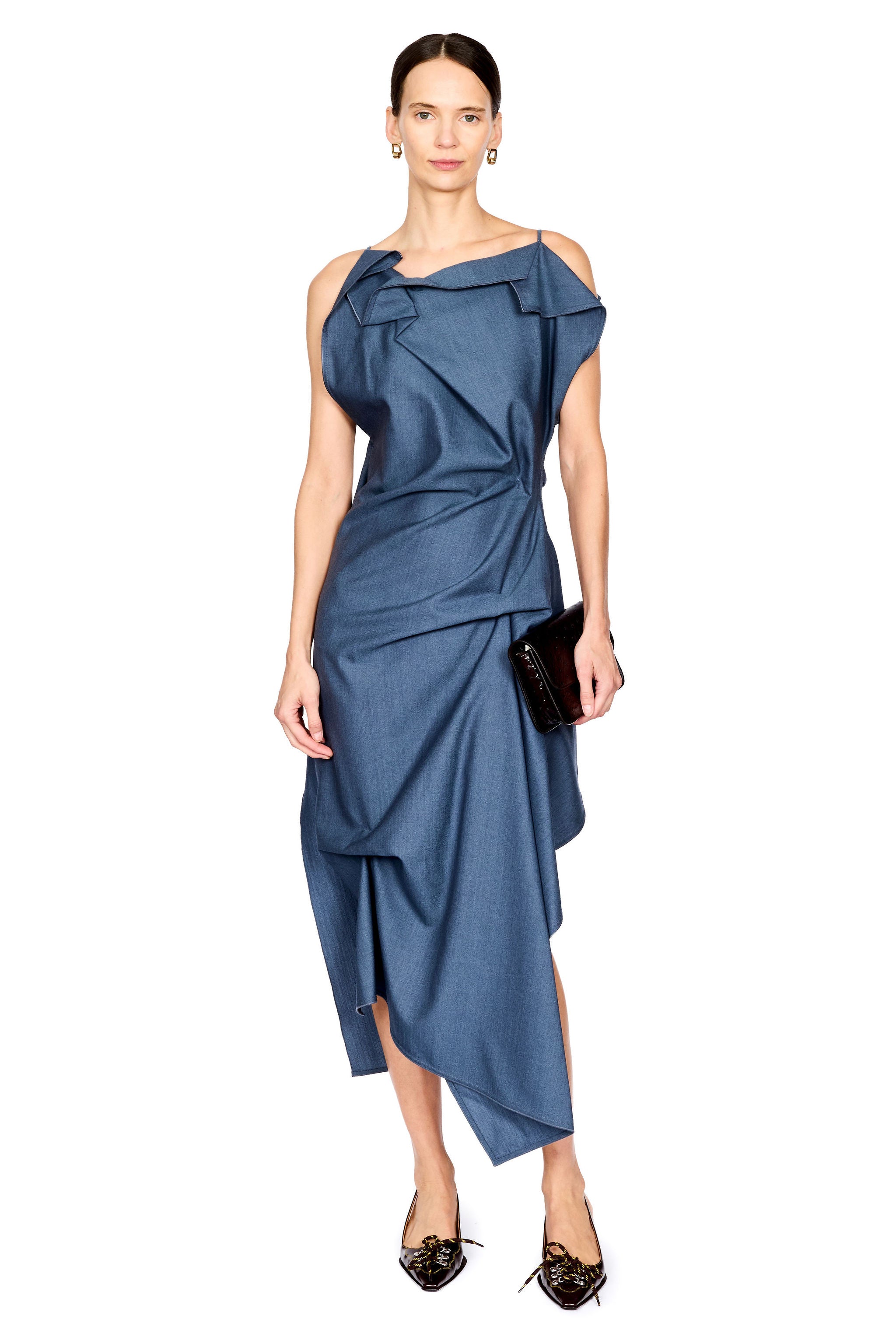 A model wearing a blue one-shoulder draped midi dress with a wrap-style skirt, holding a small black clutch against a plain white background.