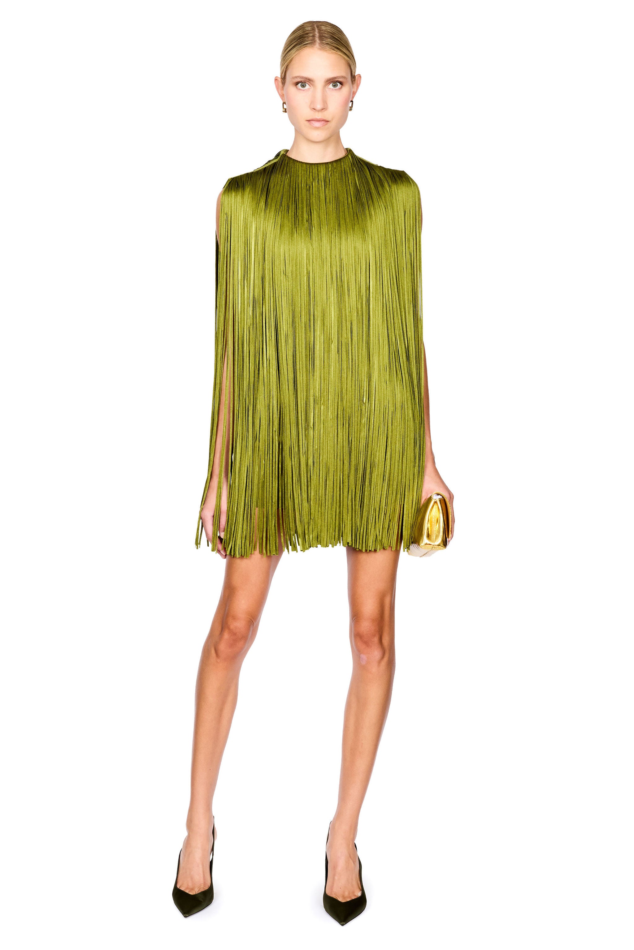 A model stands against a white background wearing a sleeveless olive green mini dress with a high mock neck, paired with dark green pointed-toe heels and holding a small gold clutch.