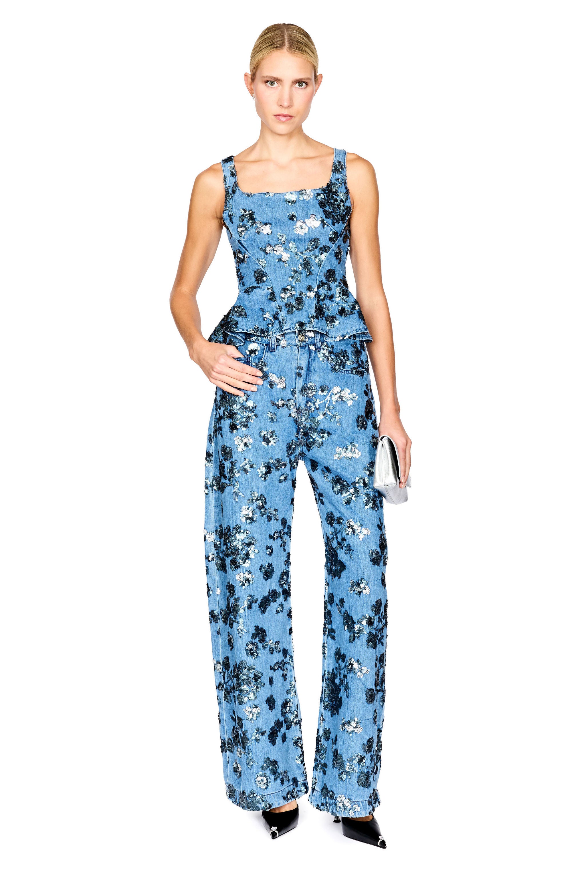 A model wearing a sleeveless denim floral top with a peplum waist with matching jeans, photographed against a solid white background.