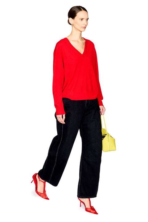 A woman modeling a bright red long-sleeve V-neck top, paired with black wide-leg trousers, red high heels, and a small yellow handbag, set against a plain white background.