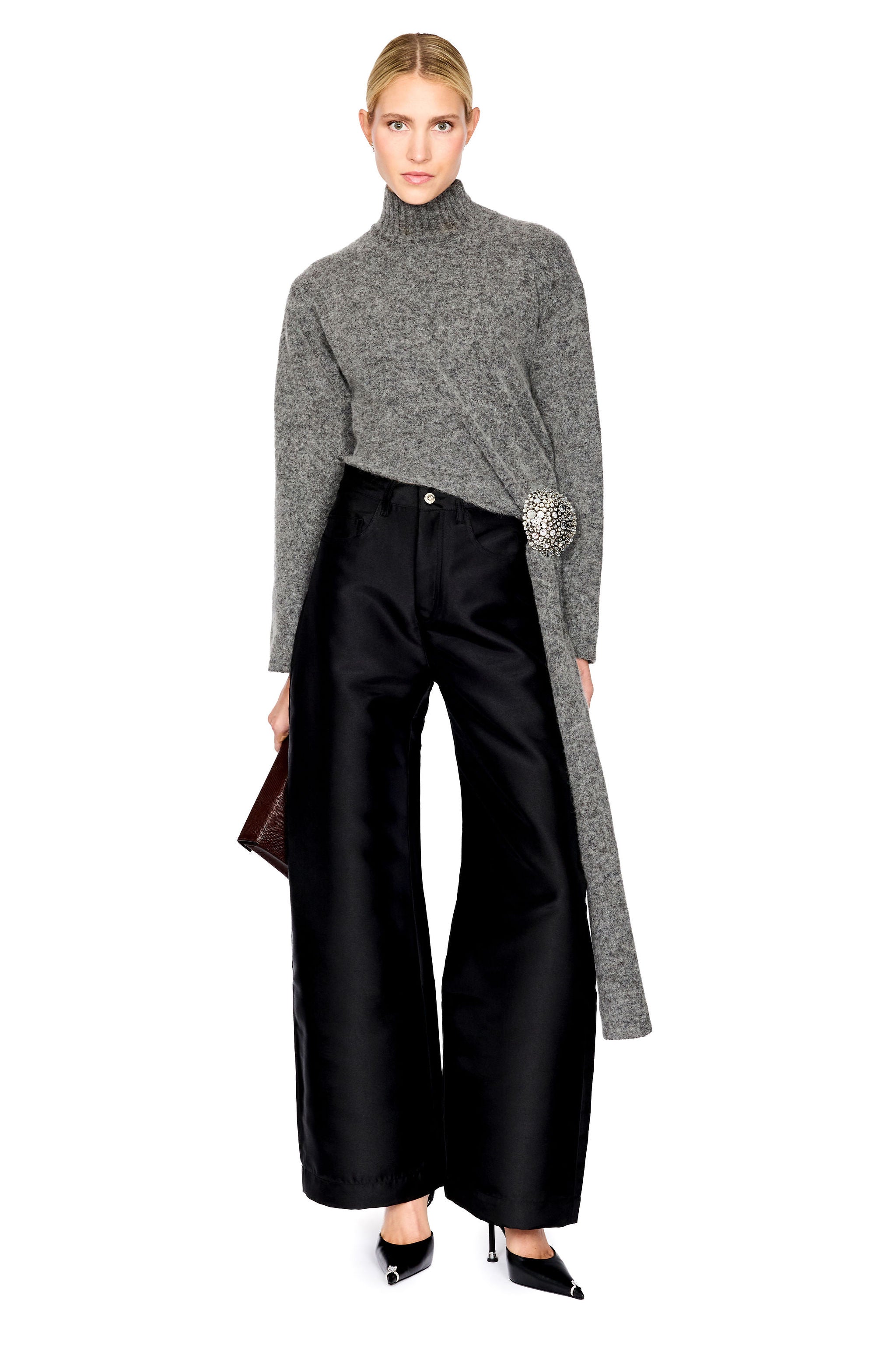 A model wearing a gray knit turtleneck sweater with a long draped overlay, paired with black wide-leg trousers and black pointed heels, against a plain white background.