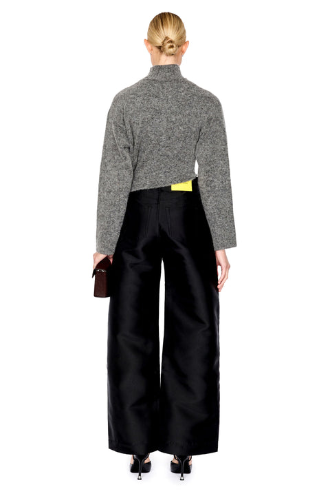 A model shown from the back wearing a gray cropped turtleneck sweater, black wide-leg trousers, and black heels, holding a small dark brown clutch against a plain white background.