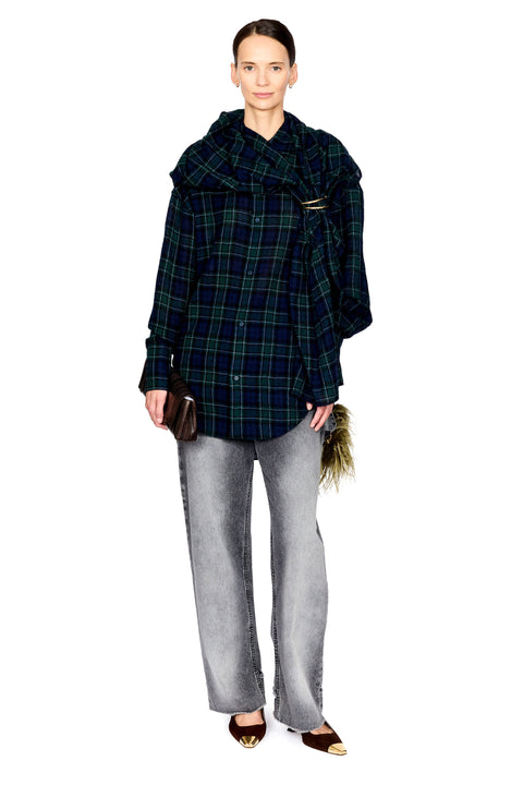 A model stands against a white background wearing a dark green and black plaid oversized button-up shirt with a wide collar, paired with light gray wide-leg jeans and brown pointed flats.