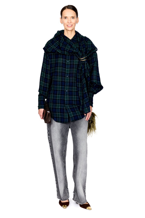 A model wearing a dark green and black plaid oversized shirt jacket with a wide collar, paired with light gray jeans and brown pointed flats with gold toe caps, against a plain white background.