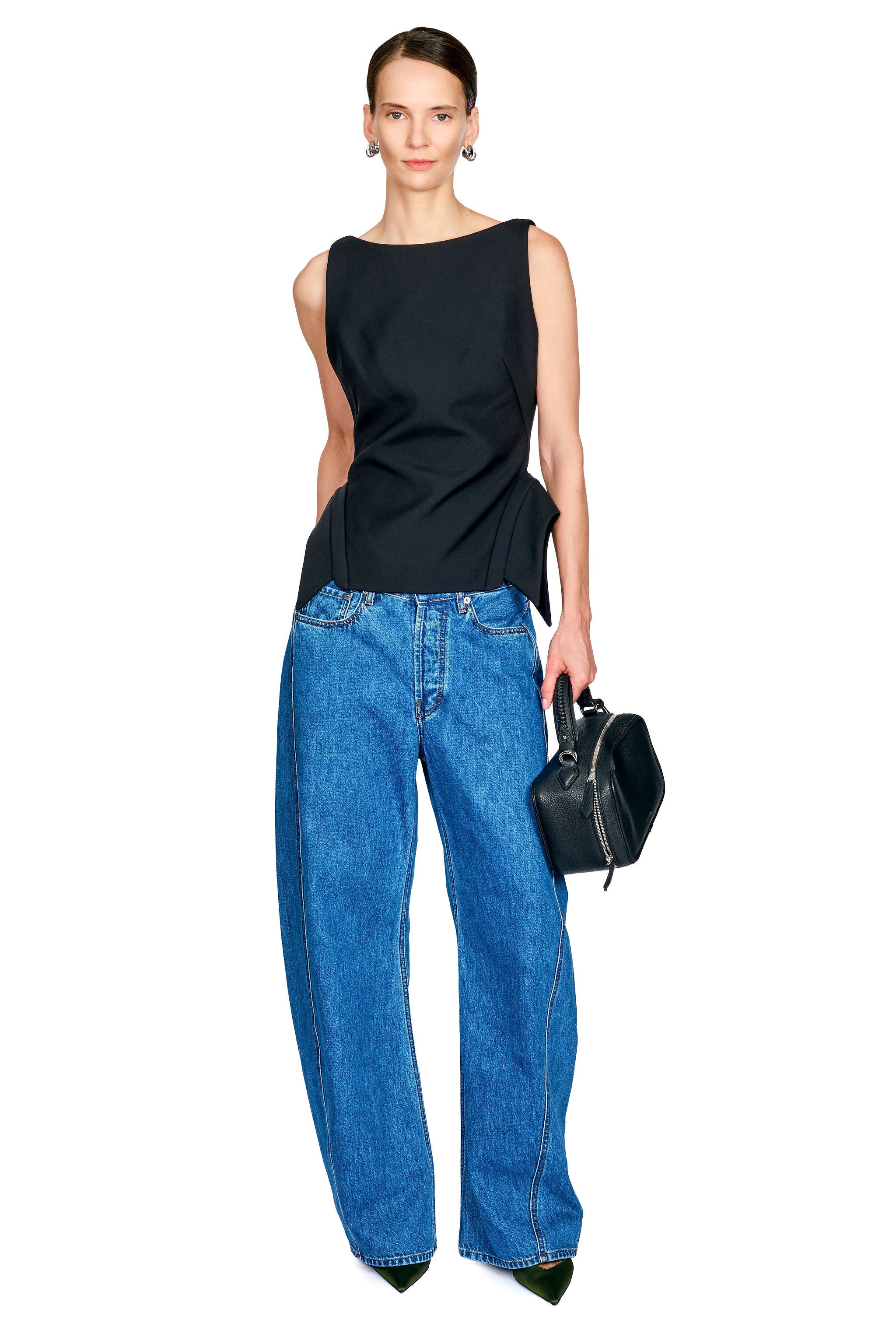 A model wearing a black sleeveless top and wide-leg blue jeans, holding a small black handbag against a plain white background.