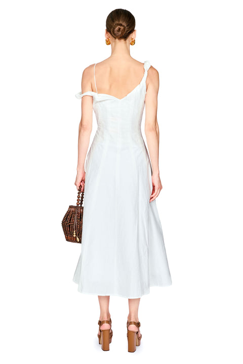 A woman shown from the back wearing a white off-the-shoulder midi dress with a fitted bodice and flared skirt, holding a brown woven handbag against a plain white background.