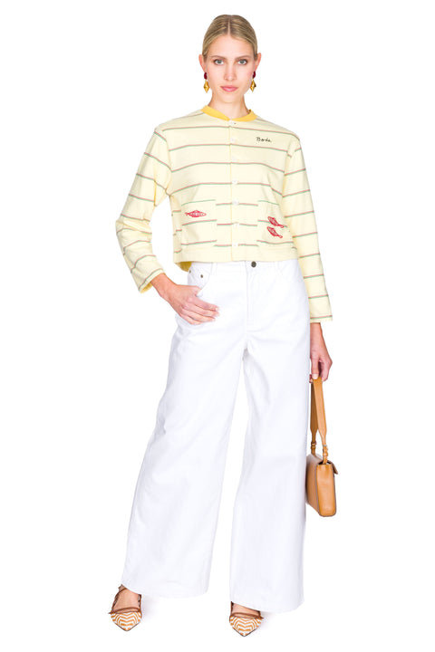 Woman wearing a yellow striped sweater with red fish on the pockets and white pants on a white background