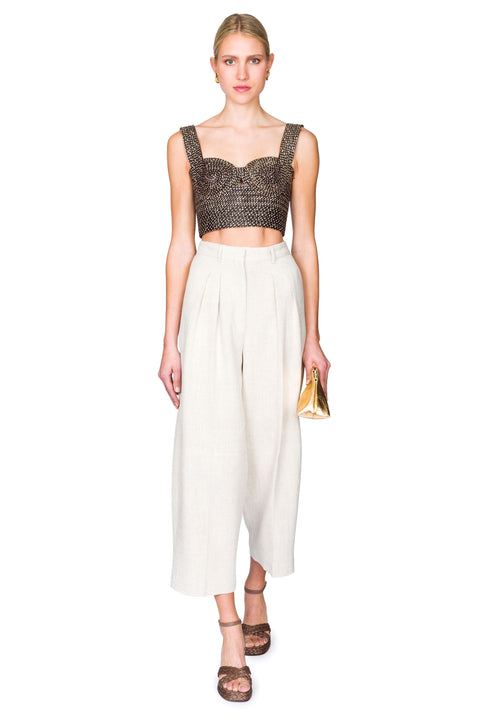 Woman stepping from the front wearing a black and tan woven  bustier crop top and white pants on a white background
