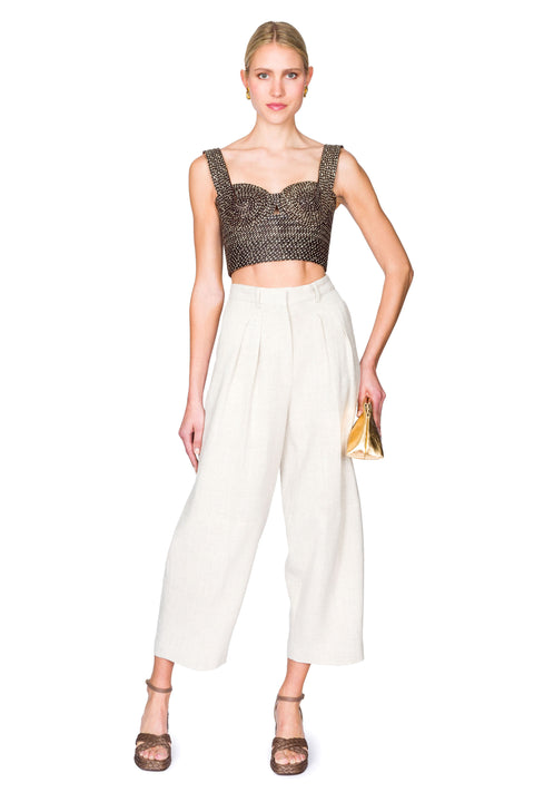 Woman posing to the side wearing a black and tan woven  bustier crop top and white pants on a white background