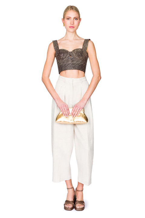 Woman clutching her bag wearing a black and tan woven  bustier crop top and white pants on a white background