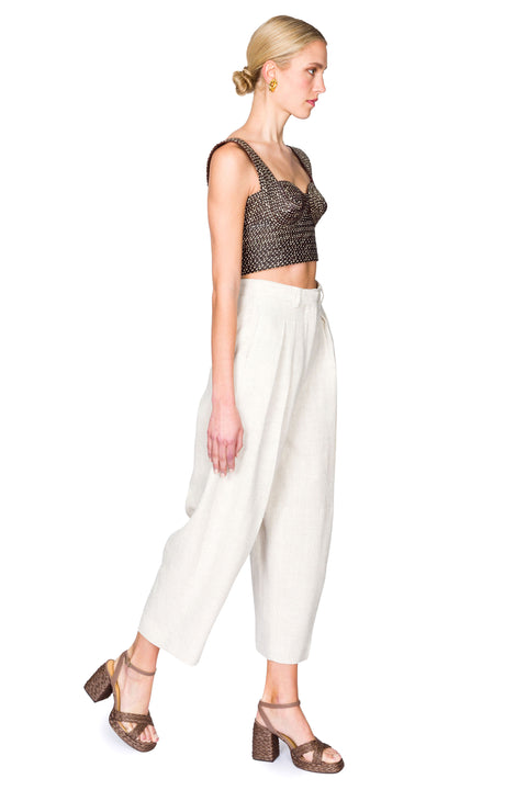 Side view of woman wearing a black and tan woven  bustier crop top and white pants on a white background