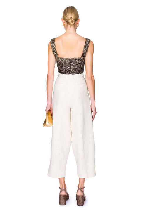 Woman from the back wearing a black and tan woven  bustier crop top and white pants on a white background