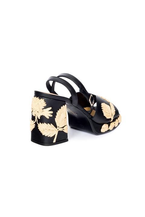View from the back of black platform sandal with woven leaf patterns on a white background.