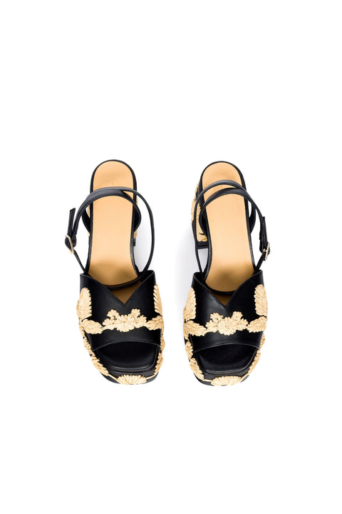 Overhead view of black platform sandal with woven leaf patterns on a white background.