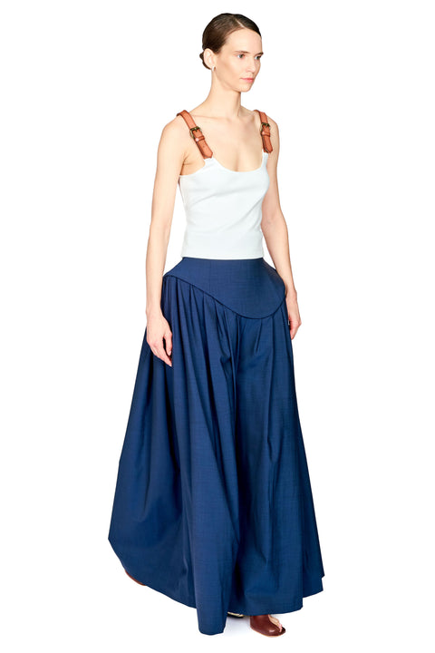 A model wearing a white sleeveless top with brown shoulder straps and a long navy blue skirt, photographed against a plain white background.