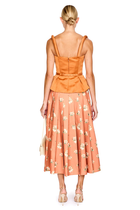 A woman shown from the back wearing a sleeveless orange peplum-style top and a peach midi skirt with a white floral print, paired with beige heels against a plain white background.
