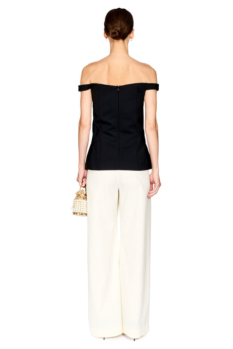 A woman shown from the back wearing an off-the-shoulder black top and wide-leg cream pants, holding a small woven handbag against a plain white background.