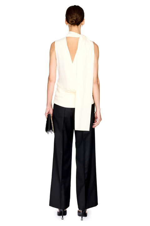 A model shown from the back wearing a sleeveless cream wrap-style top with a deep V back, black wide-leg trousers, and black heels, holding a small black clutch against a plain white background.