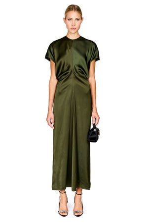 A model wearing a short-sleeved olive green satin midi dress with a gathered front detail, paired with black high-heeled sandals and a small black handbag, set against a plain white background.