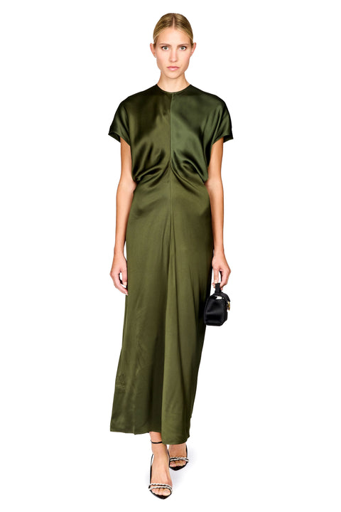 A woman modeling a short-sleeved olive green satin midi dress with a gathered front detail, paired with black high-heeled sandals and a small black handbag, against a plain white background.