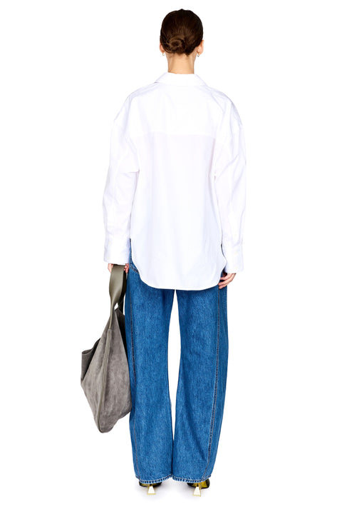 A model shown from the back wearing an oversized white button-down shirt and wide-leg blue jeans, holding a gray tote bag against a solid white background.