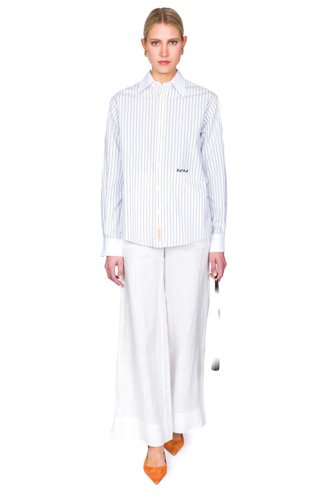 Woman wearing a striped shirt and white pants on a white background with one foot forward.