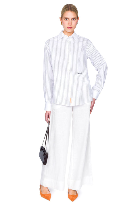 Woman wearing a striped shirt and white pants on a white background with one hand on the hip.