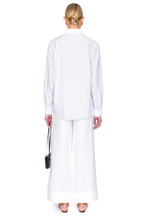 Woman wearing a striped shirt and white pants on a white background from the back.