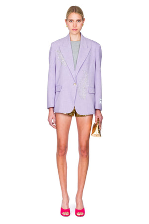 Woman wearing a light purple blazer with embellishments on a white background.