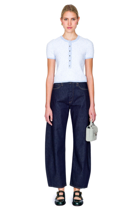 Woman wearing a light blue top with buttons and dark blue jeans on a white background posing from the front