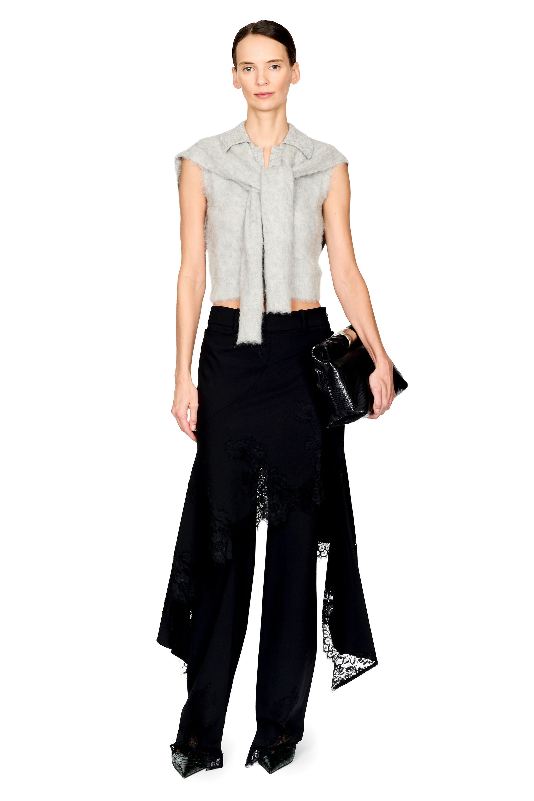 A model stands against a white studio background wearing a light gray sleeveless fuzzy wrap top with a tie detail, black wide-leg trousers with lace trim, and holding a small black clutch.