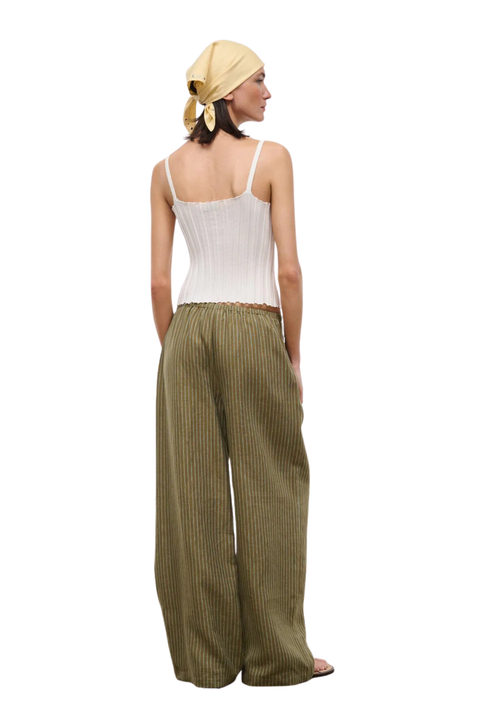 Woman wearing a white top and green striped linen beach pants on a white background back angle