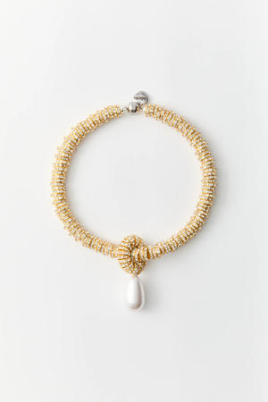 Gold beaded necklace with a white pendant on a light gray background