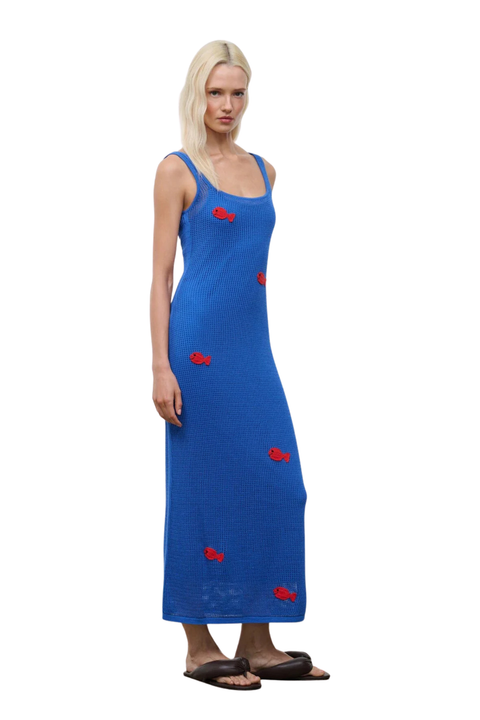 Woman wearing a blue crochet dress with red fish embroidery patterns on a white background side angle