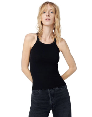 Woman wearing a black tank top and dark jeans against a plain background
