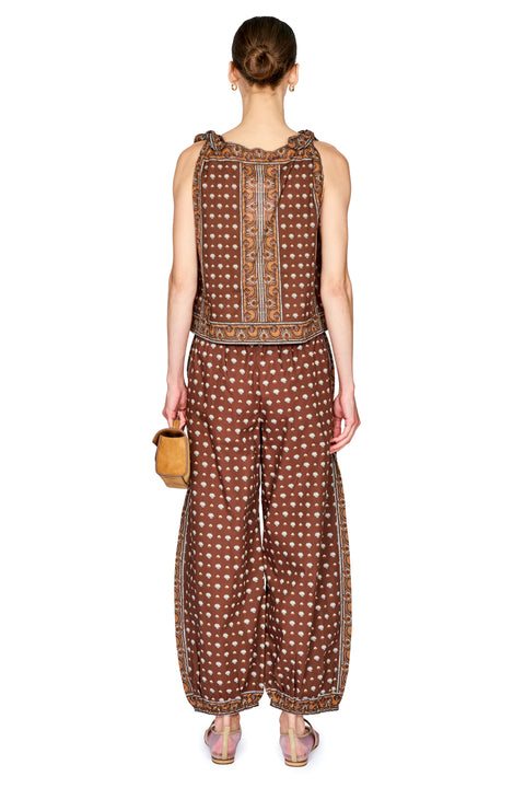 A model shown from the back wearing a matching brown and white patterned sleeveless top and wide-leg pants set, holding a small tan handbag against a plain white background.