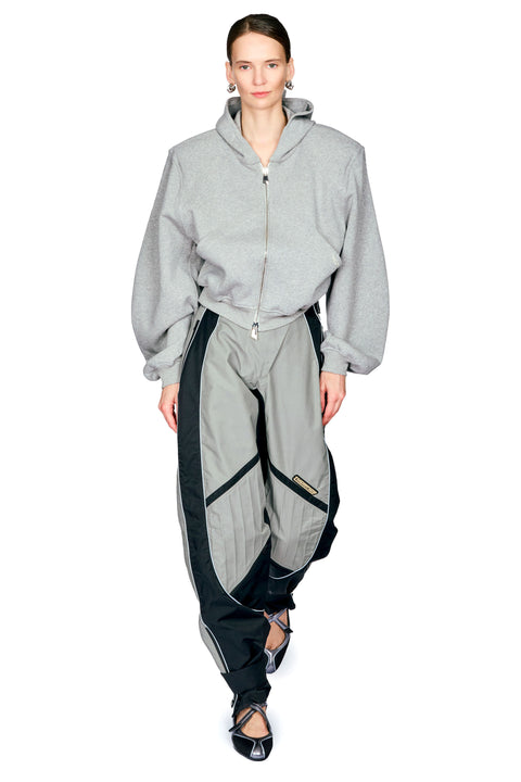 A model wearing a light gray zip-up hooded sweatshirt and matching gray cargo pants with black side panels, photographed against a plain white studio background.