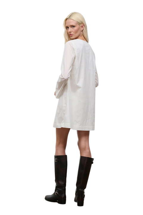 The back angle of a woman wearing a low cut, long sleeve white mini dress