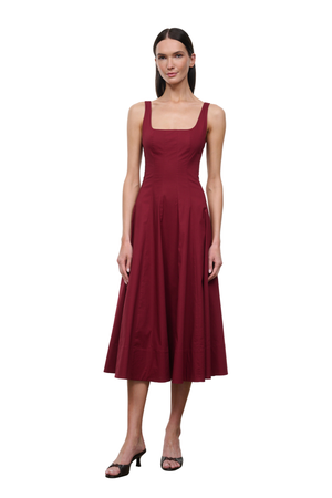 A woman modeling a sleeveless midi dress in deep burgundy with a square neckline and a flared skirt, paired with black heeled sandals, against a plain white background.
